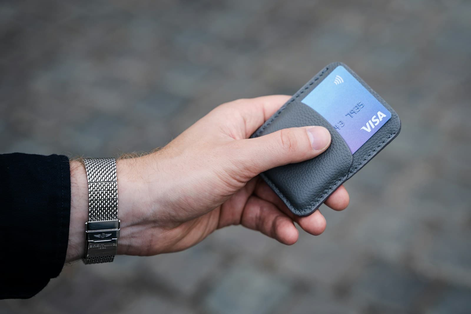 Un porte-cartes en cuir gris tenu à deux mains, dont dépassent plusieurs cartes de paiement.