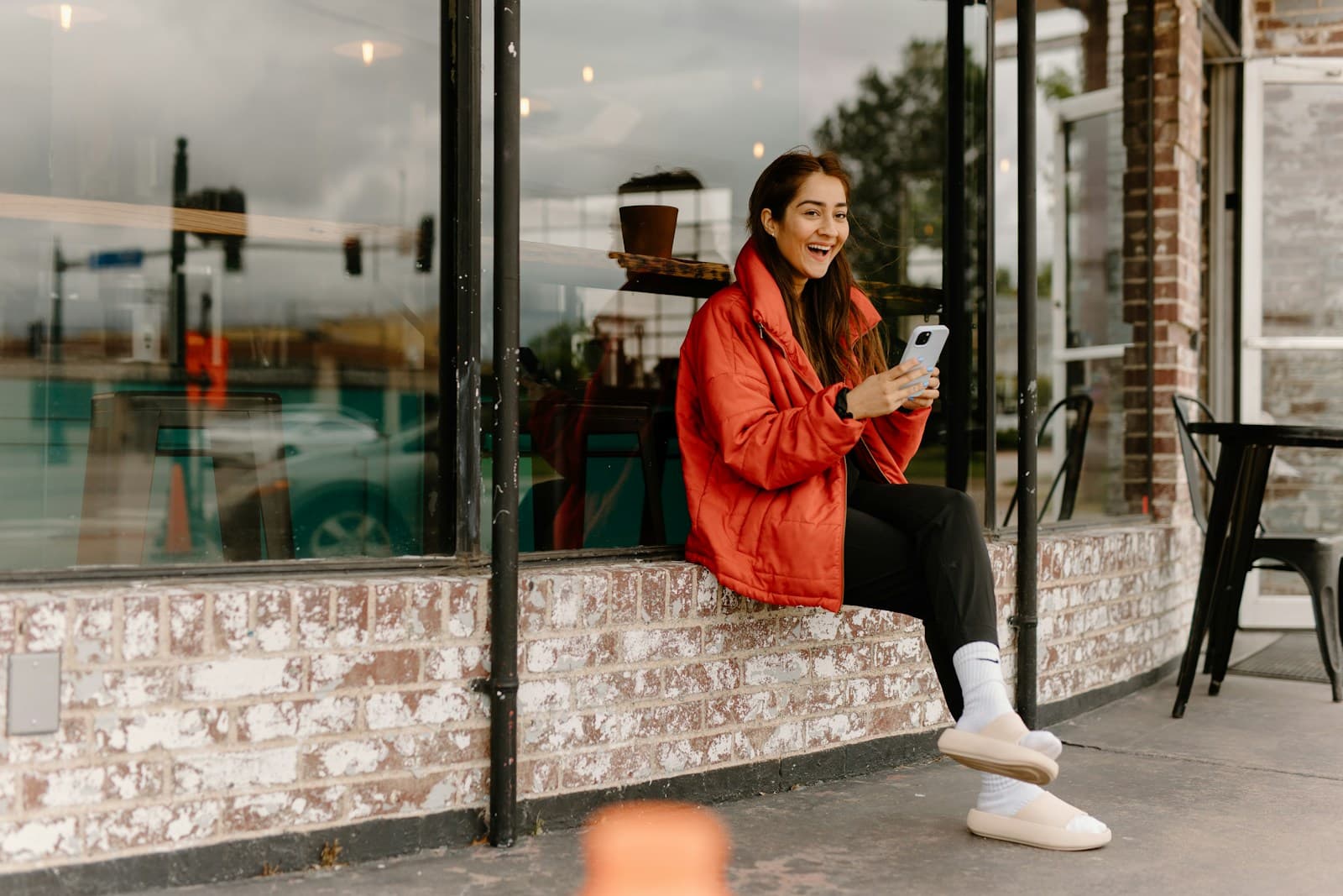 Une femme assise sur un rebord de fenêtre regarde son téléphone, dans la lumière d'une rue.