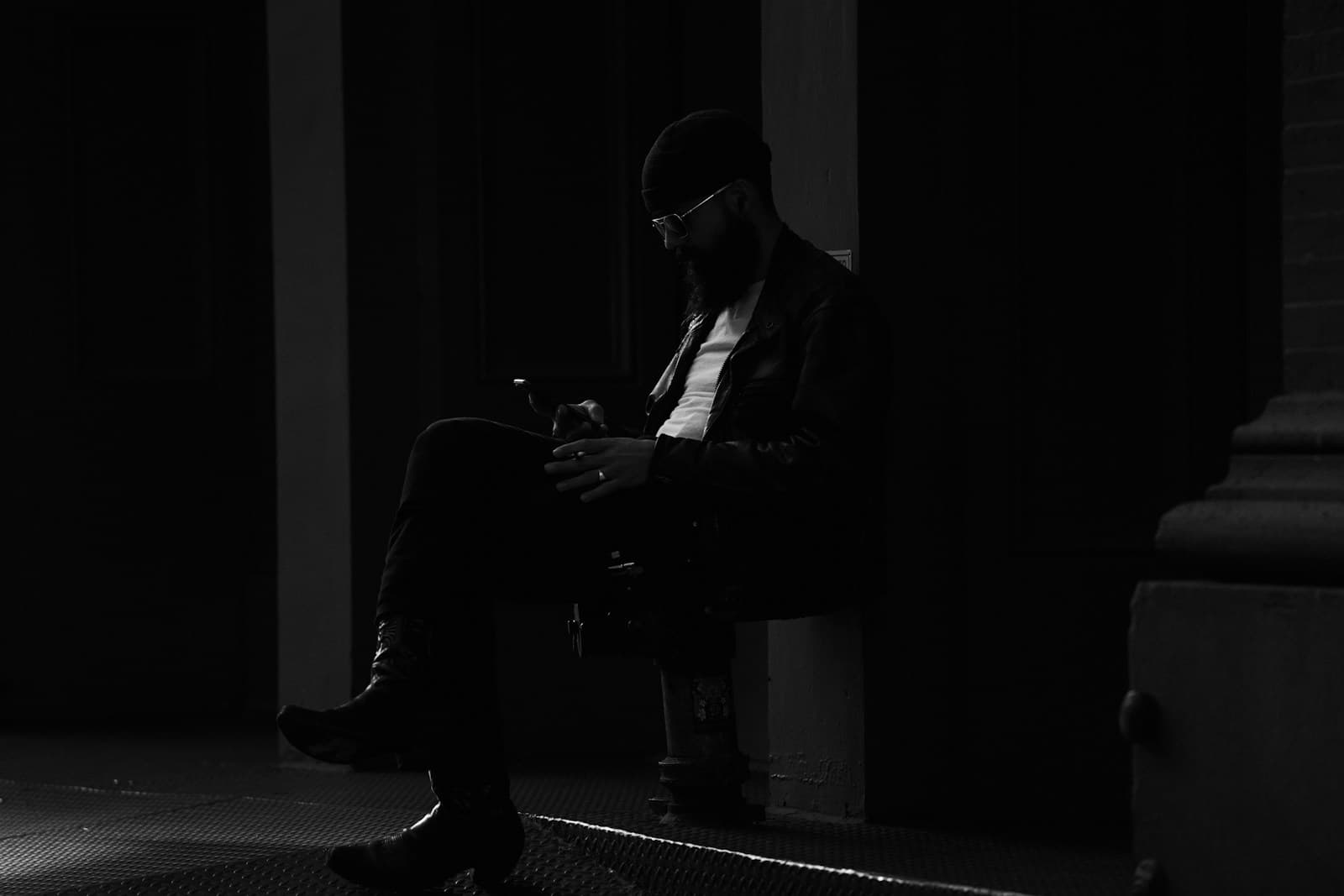 Un homme assis sur une chaise, dehors, consulte l'écran de son téléphone.